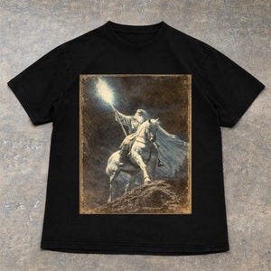 Black Vintage Gandalf on horseback with glowing staff in a vintage fantasy illustration, lord of the rings inspired wizard design, lotr fan art style graphic tee, magical wizard scene with detailed horse and mystical light, fantasy lover gift, wizard gift idea, lord of the ring shirt, gandalf shirt, fantasy aesthetic clothing, unisex streetwear tee, high quality print, perfect gift for lotr fans and magic lovers
