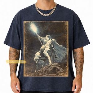 Navy Vintage Gandalf on horseback with glowing staff in a vintage fantasy illustration, lord of the rings inspired wizard design, lotr fan art style graphic tee, magical wizard scene with detailed horse and mystical light, fantasy lover gift, wizard gift idea, lord of the ring shirt, gandalf shirt, fantasy aesthetic clothing, unisex streetwear tee, high quality print, perfect gift for lotr fans and magic lovers