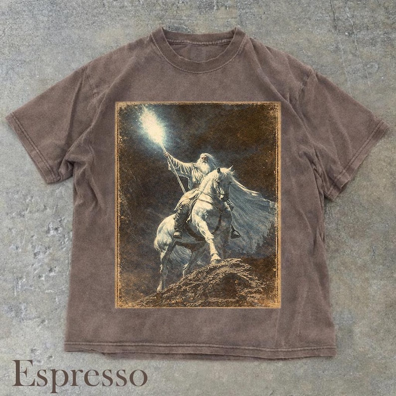 Puede incluir: Camiseta color espresso con una ilustraci&oacute;n vintage de un mago a caballo sosteniendo un bast&oacute;n brillante. El gr&aacute;fico tiene un borde desgastado. La camiseta tiene cuello redondo y mangas cortas.
