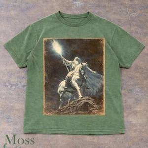 Moss t-shirt featuring Gandalf wizard riding a horse with glowing staff, Lord of the Rings Tolkien inspired Middle-earth fantasy design, vintage style wizard illustration artwork, epic adventure graphic tee for fantasy lovers and LOTR fans, wizard aesthetic clothing, unisex streetwear, mystical light and dark theme apparel, detailed character design, magical atmosphere shirt, perfect fantasy gift idea for him and her