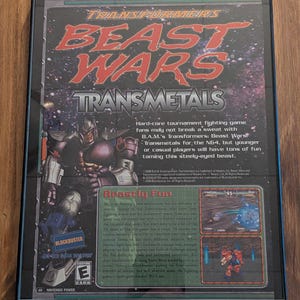 May include: Framed Transformers: Beast Wars Transmetals video game poster. The poster features the game's title in red and the image of a robot. The Blockbuster logo and the ESRB rating are also visible.