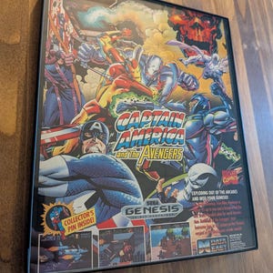 Puede incluir: Cartucho de juego Sega Genesis enmarcado para "Captain America and The Avengers". La car&aacute;tula presenta ilustraciones de estilo c&oacute;mic de Capit&aacute;n Am&eacute;rica, Iron Man y otros personajes de los Vengadores. El t&iacute;tulo del juego se muestra de forma destacada.