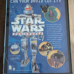 Könnte beinhalten: Eine Star Wars Droidworks PC-Spielbox. Das Box-Art zeigt einen großen Roboter mit dem Text "CAN YOUR DROID CUT IT?" und dem Star Wars-Logo. Zusätzlicher Text enthält "DESIGN", "DEPLOY" und "OUTSMART".