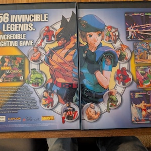 May include: Marvel vs. Capcom fighting game case featuring Wolverine and a female character in a blue uniform. The case includes the game disc and character art. Text reads "56 Invincible Legends. 1 Incredible Fighting Game."