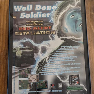 May include: Framed poster for the video game "Command & Conquer: Red Alert Retaliation." The artwork features a soldier's face with lightning, a military vehicle, and game screenshots. Text includes "Well Done Soldier" and game details.