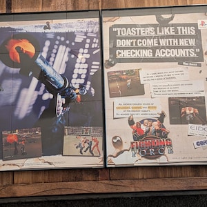 May include: Two framed posters featuring artwork and text. One poster has a futuristic cityscape with a large object in the center. The other poster has the text "TOASTERS LIKE THIS DON'T COME WITH NEW CHECKING ACCOUNTS."