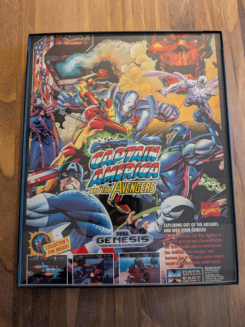 Puede incluir: Un cartucho de videojuego Sega Genesis enmarcado para "Captain America and The Avengers". La car&aacute;tula presenta a Capit&aacute;n Am&eacute;rica, Iron Man y otros personajes de Marvel en acci&oacute;n. El juego es un t&iacute;tulo de Marvel Comics.