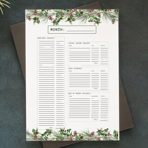 Puede incluir: Una página de planificador blanca con un borde festivo de agujas de pino verdes y bayas rojas. La página está sobre una superficie negra, rodeada de ramas de pino y piñas. En la parte superior está la palabra "MONTH:" sobre un espacio en blanco.