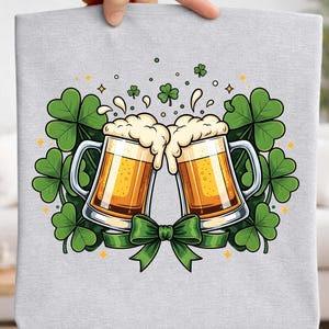 May include: A light gray tote bag featuring a St. Patrick's Day design. Two mugs of beer are clinking together, surrounded by green shamrocks, a green bow, and golden accents. The design is festive and celebratory.
