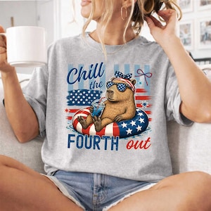 May include: A gray sweatshirt with a graphic of a capybara wearing sunglasses and a patriotic headband, floating on a red, white, and blue inner tube. The text reads "Chill the Fourth out."