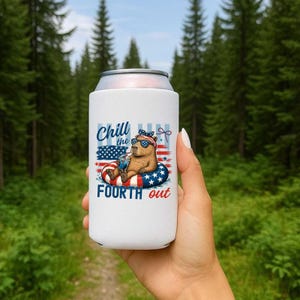 May include: White can cooler featuring a capybara wearing sunglasses and a patriotic headband, floating on a red, white, and blue inner tube. The text "Chill the Fourth out" is displayed on the cooler, with an American flag design.