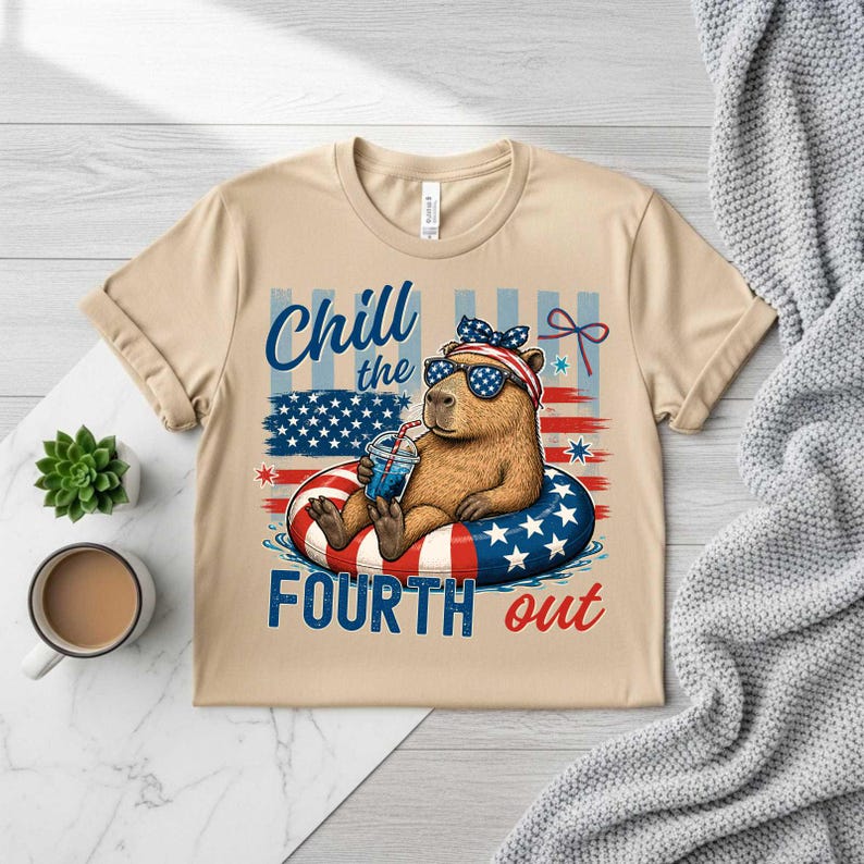 May include: Beige t-shirt featuring a cartoon capybara wearing sunglasses and a patriotic headband, relaxing in a red, white, and blue inner tube. The shirt has the text "Chill the Fourth out" in blue and red.
