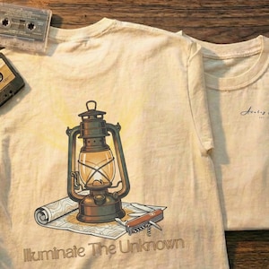 May include: Two cream-colored t-shirts with a vintage lantern graphic and the text "Illuminate The Unknown." The image includes cassette tapes, a camera, and floppy disks, suggesting a retro theme.