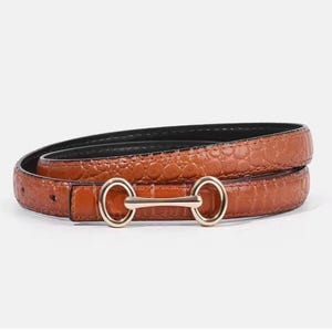 May include: A thin tan belt with a textured crocodile skin pattern and a gold-toned metal horsebit buckle. The belt is coiled into a circular shape, showcasing the embossed leather-like surface and the polished metallic hardware detail.