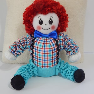 May include: A handmade rag doll with red curly hair, a blue bow tie, a plaid shirt, and blue ruffled pants.