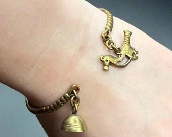 May include: A gold-toned metal bracelet with a bell charm and a horse-shaped charm. The bracelet has a textured, twisted design. The bell charm is a small, rounded shape. The horse charm is a stylized silhouette.