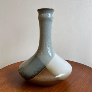 Op de afbeelding: Een keramische vaas met een brede, ronde basis en een lange, smalle hals. De vaas is versierd met een geometrisch patroon in bruin, grijs en wit.