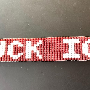 May include: A beaded bracelet with the words "FUCK ICE" in white letters against a red background. The bracelet has silver-colored metal ends.