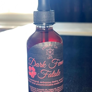 May include: A dark red glass bottle with a black dropper and a black label. The label reads "HOUSE OF" above "Dark Femme Fatale" in pink script. The bottle contains 2 fl oz of liquid.