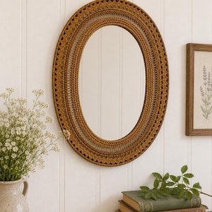 May include: An oval wall mirror featuring a decorative frame crafted from brown woven cord. The frame displays intricate macrame-style knotting patterns arranged in concentric circles around the central reflective glass surface.