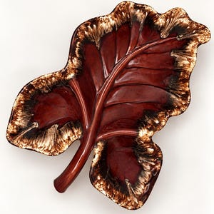 May include: A ceramic dish shaped like a large leaf with a glossy finish. The center is a deep, rich mahogany brown, while the scalloped edges feature a decorative blend of cream, tan, and dark brown glaze with a textured, drip-like appearance.
