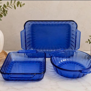 Puede incluir: Un juego de tres fuentes de horno de cristal azul cobalto con textura acanalada en los laterales y asas integradas. La colección incluye una fuente rectangular grande, una cuadrada más pequeña y una redonda con base estriada.