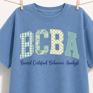 Könnte beinhalten: Ein blaues T-Shirt in Jeansoptik mit den Buchstaben BCBA in College-Schriftart und verschiedenen Mustern wie blauem Vichy-Karo, Blumen, Punkten und Streifen. Unter den Buchstaben steht der Text Board Certified Behavior Analyst.