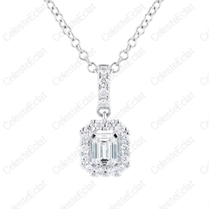 Puede incluir: Un collar de tono plateado con una piedra central rectangular de corte esmeralda rodeada por un halo de pequeñas piedras redondas. El colgante cuelga de una cadena delicada e incluye un pasador vertical adornado con piedras redondas.