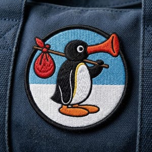 May include: Embroidered patch featuring a cartoon penguin with a red bag on a stick and a large orange horn. The penguin is black and white with orange feet, set against a blue and white background, all within a circular black border.