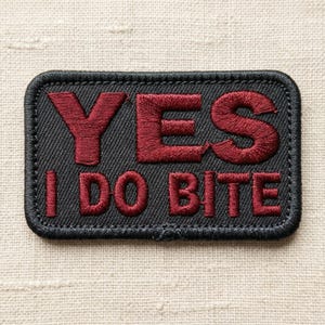 May include: A white ceramic mug with a black handle and the text "But First, Coffee" in a bold, black font. The mug is set against a blurred background, suggesting a cozy setting.