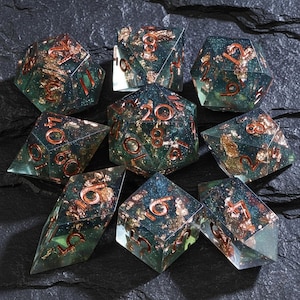 May include: A set of nine polyhedral dice. The dice are clear with a teal hue, filled with gold flakes, and feature copper-colored numbers. The dice are arranged on a dark, textured surface.