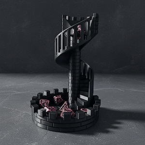 May include: Black dice tower featuring a spiral staircase design. The tower has a circular base with crenellations and holds several red and black dice. The tower is made of a dark material and is set against a dark background.