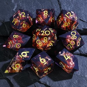 May include: A set of nine polyhedral dice for tabletop games. The dice are a deep purple with gold numbering and a fiery, amber-colored interior. The dice are arranged on a dark, textured surface.