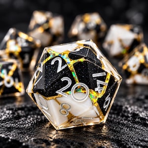 May include: A twenty-sided die featuring a segmented design of opaque black and white resin pieces separated by thin, shimmering gold foil veins. The numbers are etched in a clean, sans-serif font and filled with a metallic silver pigment.