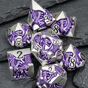 May include: A set of seven polyhedral dice featuring a silver metal finish with recessed purple enamel dragon motifs. Each die displays black engraved numbers, including a twenty-sided die, a twelve-sided die, and various other geometric shapes.