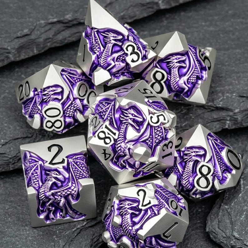 May include: A set of seven polyhedral dice featuring a silver metal finish with recessed purple enamel dragon motifs. Each die displays black engraved numbers, including a twenty-sided die, a twelve-sided die, and various other geometric shapes.