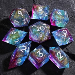 May include: A collection of eight multi-sided dice with a galaxy design. The dice feature blue, purple, and gold glitter, with white numerals. These dice are for tabletop role-playing games.