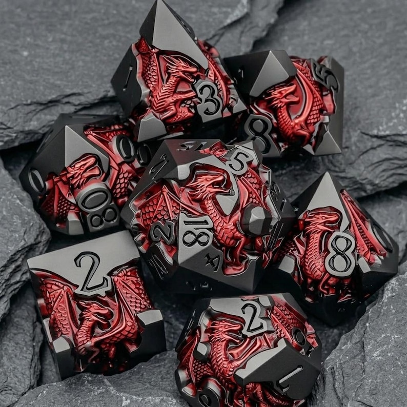 May include: A set of seven polyhedral dice featuring a matte black finish with metallic red dragon reliefs integrated into each face. The numbers are engraved in a clear, bold font, contrasting against the dark metal surfaces of the dice.