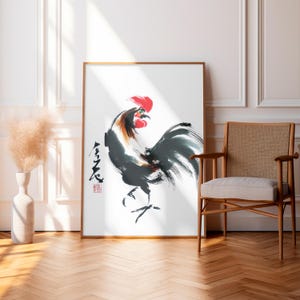 Puede incluir: Una impresión artística enmarcada con una pintura de acuarela de un gallo. El gallo está representado en negro, gris y marrón con una cresta roja. La obra de arte incluye caligrafía japonesa y un sello rojo. La impresión se exhibe en una habitación con suelo de madera y una silla.