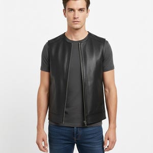 K&ouml;nnte beinhalten: Eine schwarze Lederweste mit durchgehendem Rei&szlig;verschluss, getragen &uuml;ber einem grauen Rundhals-T-Shirt. Die Weste hat eine ma&szlig;geschneiderte Passform und ein subtiles, strukturiertes Aussehen. Die Person tr&auml;gt blaue Jeans.