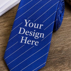 以下が含まれることがあります： 白の斜めストライプと「Your Design Here」の文字が入った青いネクタイ。ネクタイは端が丸まっており、木製の表面に置かれています。背景には白いシャツが見えます。