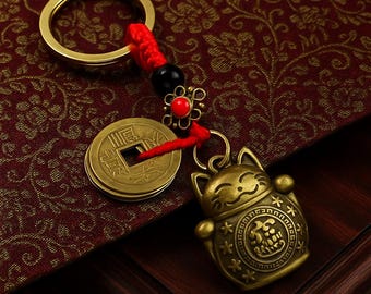 May include: A gold-colored keychain featuring a lucky cat charm, Chinese coins, and a red cord. The keychain includes a round key ring and a decorative flower with a red gem. The text "KEYVERSEGIFTS" is at the bottom.