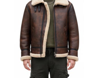 Puede incluir: Chaqueta de cuero marrón con cuello y forro de borrego color crema. La chaqueta tiene cremallera, dos bolsillos delanteros y una correa abrochada en el cuello. Estilo aviador clásico.