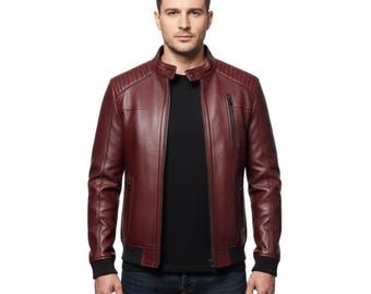 Puede incluir: Chaqueta de cuero burdeos con diseño de hombros acanalados y cremallera negra. La chaqueta tiene cuello alzado y puños negros. El modelo lleva una camiseta negra y vaqueros azules.
