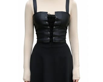 May include: Black faux leather corset top with adjustable straps and a lace-up front. The top is paired with a black skirt and a beige turtleneck long-sleeve shirt. The corset has a square neckline and a structured design.