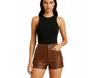 Op de afbeelding: Een zwarte mouwloze top gecombineerd met bruine leren shorts. De shorts hebben een klassiek ontwerp met vijf zakken en een knoopsluiting. Het model draagt de outfit.
