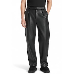 Op de afbeelding: Zwarte leren broek met bijpassende riem. De broek heeft een geplooide voorkant en een wijde pijp. De riem is zwart en past bij de broek. De broek wordt gedragen met zwarte schoenen. De algehele stijl is modern en strak.