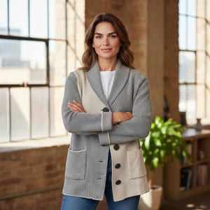 May include: A gray, beige, and white color-blocked cardigan with a shawl collar and button closure. The cardigan has two front pockets and white trim. The person is wearing a white t-shirt and blue jeans.