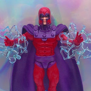 Peut inclure: Figurine de Magneto dans une pose dynamique, vêtu d'un costume rouge et violet avec un casque. La figurine tient deux effets d'énergie bleus translucides. L'arrière-plan présente un dégradé de couleurs douces.