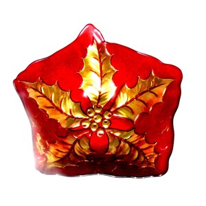 May include: A red, star-shaped decorative dish with a gold holly leaf design. The dish has a glossy finish and is likely made of glass or ceramic. The holly leaves are detailed with gold accents, and the center features small gold berries.